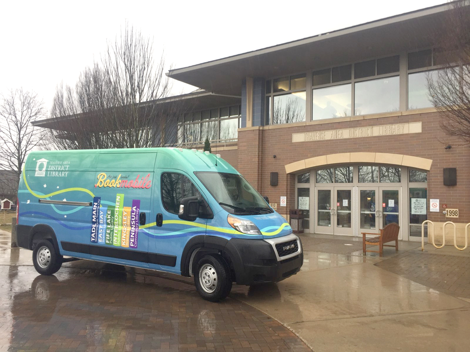 The green and blue bookmobile van parked outside the front door of the Main Library