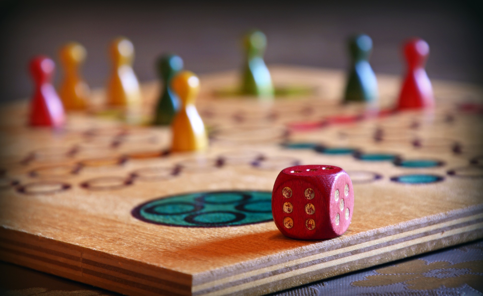 Photo of colorful gaming pieces on a wooden board with dots and a single red six-sided die